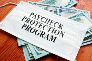 Mask layered on cash with the words "Paycheck Protection Program" typed on the mask.