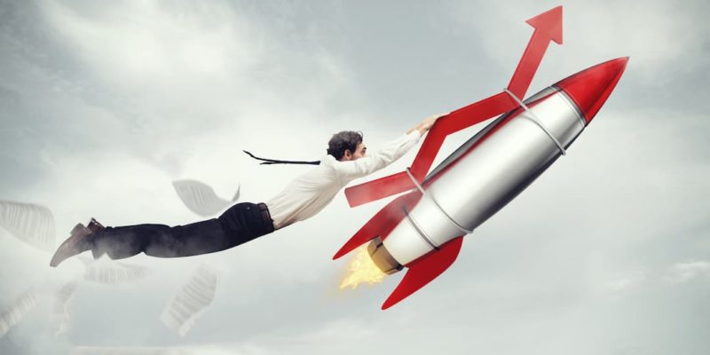 Business person holding onto an rocket in flight to illustrate increased productivity.