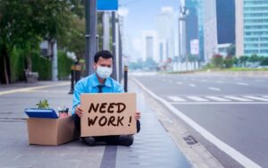 Person in business attire holding a sign that reads "need work" to illustrate a blog post about business trends in 2026 where one of the trends is economic uncertainty.