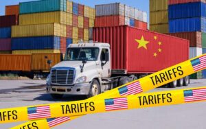 Truck surrounded by freight cars and tape with the words "tariffs" on it, to illustrate the supply chain challenges expected among the 2026 business trends.